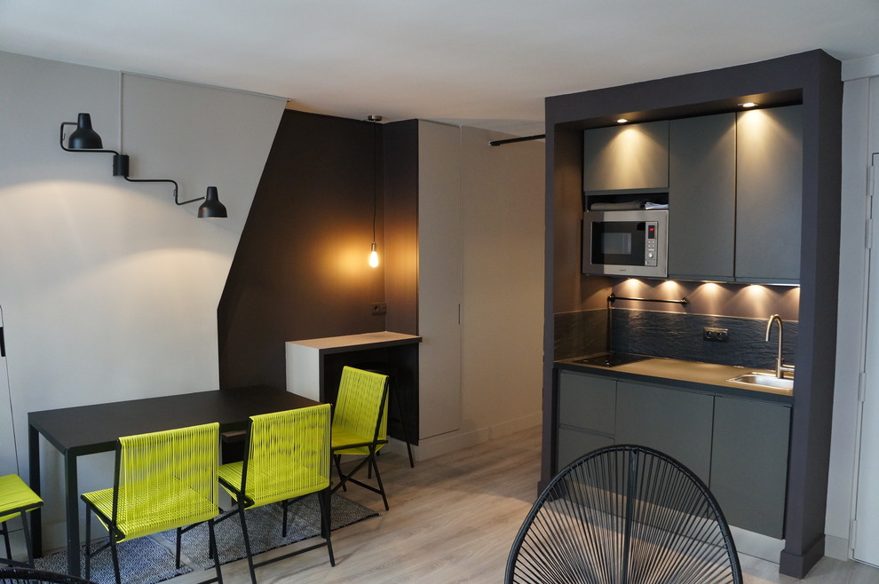 Photo of a small contemporary single-wall eat-in kitchen in Paris with a drop-in sink, black cabinets, black splashback, stone slab splashback, stainless steel appliances and light hardwood floors.