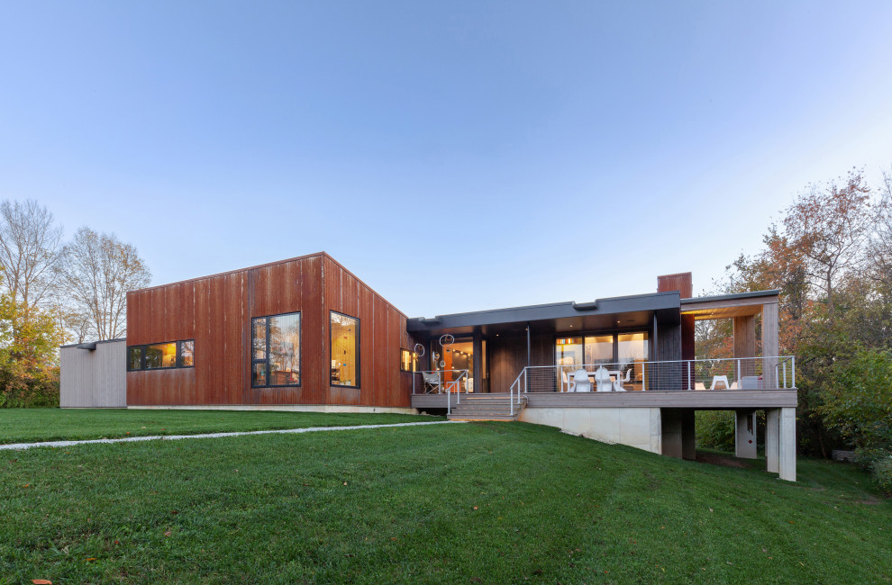 Ispirazione per la facciata di una casa arancione moderna a un piano di medie dimensioni con rivestimento in metallo, copertura in metallo o lamiera, tetto grigio e terreno in pendenza