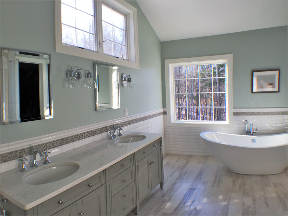 Example of a large transitional master white tile and subway tile porcelain tile freestanding bathtub design with shaker cabinets, gray cabinets, a one-piece toilet, blue walls, an undermount sink and quartz countertops