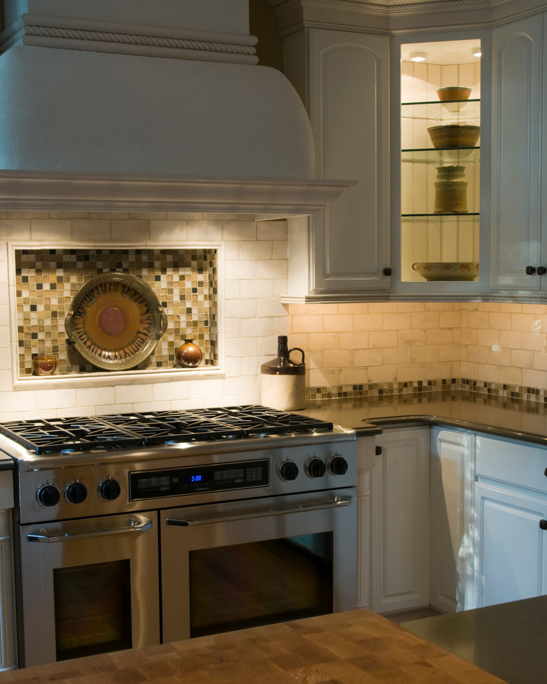 Foto på ett lantligt kök, med en undermonterad diskho, vita skåp, granitbänkskiva, vitt stänkskydd, stänkskydd i tunnelbanekakel, rostfria vitvaror, mellanmörkt trägolv och en köksö