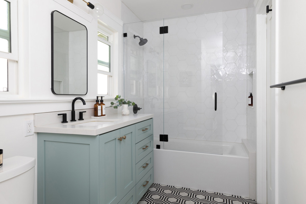 На фото: главная ванная комната среднего размера в стиле ретро с фасадами в стиле шейкер, зелеными фасадами, ванной в нише, душем в нише, унитазом-моноблоком, белой плиткой, керамогранитной плиткой, белыми стенами, полом из мозаичной плитки, врезной раковиной, столешницей из искусственного кварца, разноцветным полом, душем с распашными дверями, белой столешницей, нишей, тумбой под одну раковину и встроенной тумбой с