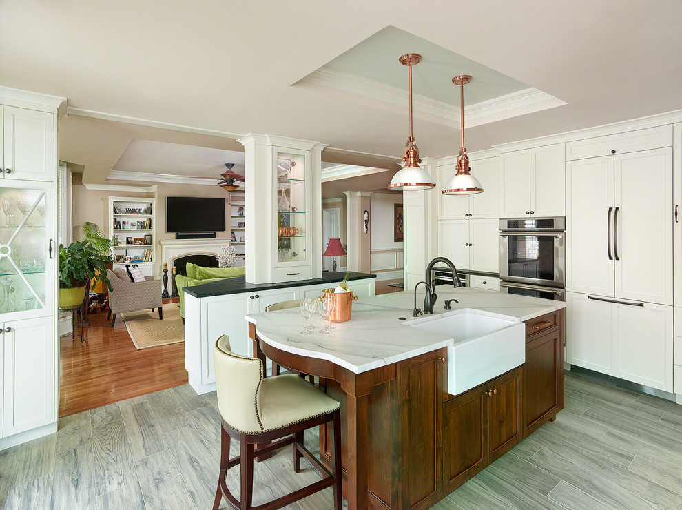 Design ideas for a mid-sized transitional kitchen in Charleston with a farmhouse sink, recessed-panel cabinets, stainless steel appliances, light hardwood floors, with island and white cabinets.