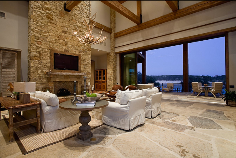 This is an example of a large country living room in Austin with beige walls, limestone floors, a standard fireplace, a stone fireplace surround and a concealed tv.