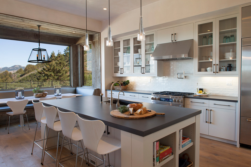 Inspiration for a contemporary eat-in kitchen in San Francisco with an undermount sink, glass-front cabinets, white cabinets, white splashback, subway tile splashback, stainless steel appliances, medium hardwood floors and with island.
