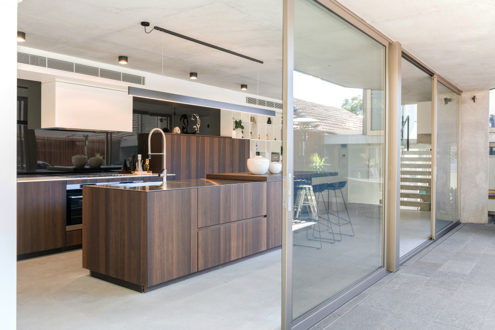 Inspiration for a large contemporary l-shaped eat-in kitchen in Sydney with an undermount sink, flat-panel cabinets, medium wood cabinets, black splashback, glass sheet splashback, panelled appliances, porcelain floors, with island, grey floor and beige benchtop.