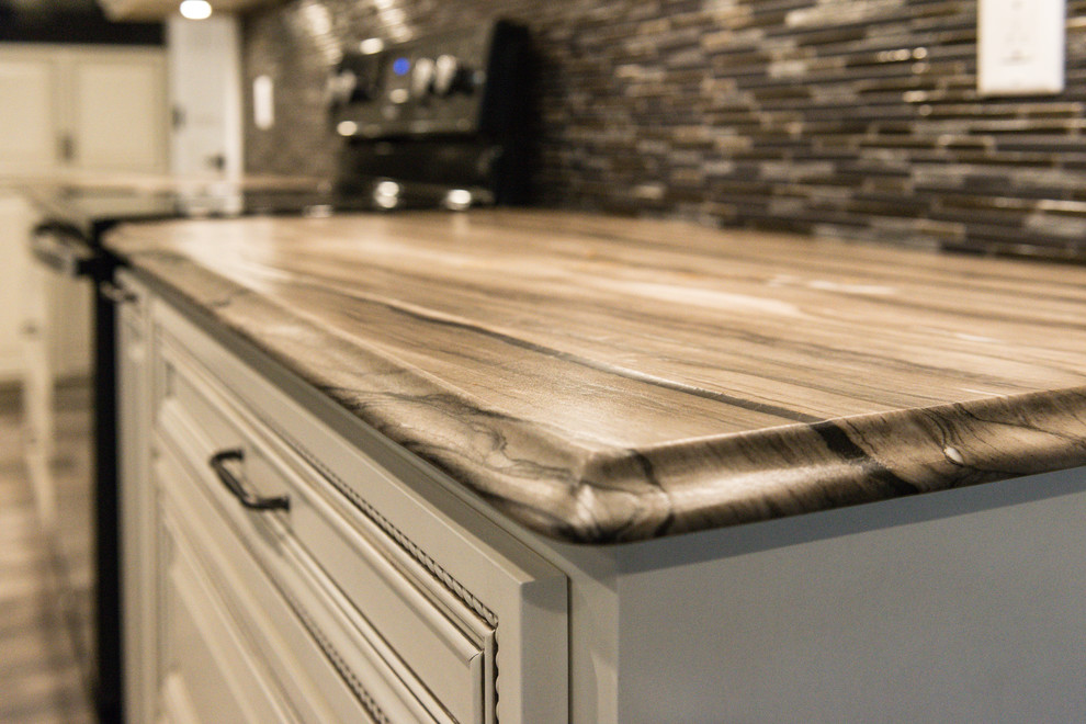 Inspiration for a large transitional l-shaped ceramic tile eat-in kitchen remodel in Chicago with an undermount sink, raised-panel cabinets, dark wood cabinets, marble countertops, brown backsplash, glass tile backsplash, black appliances and an island