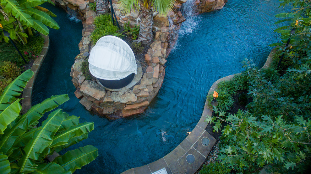 Photo of a large tropical backyard custom-shaped pool in Dallas with a water feature and natural stone pavers.