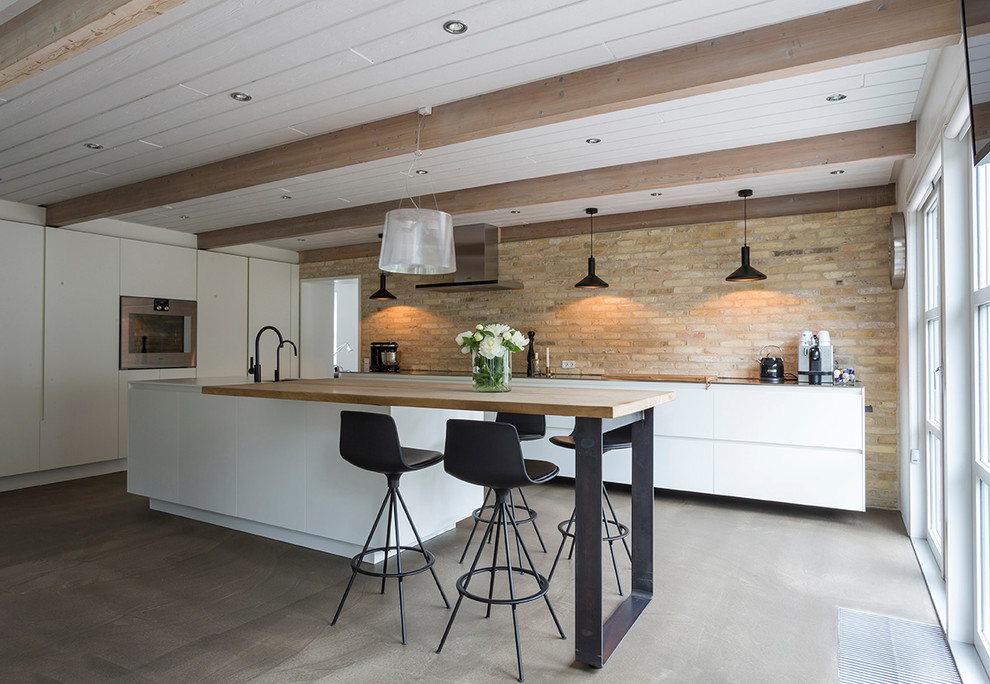 This is an example of a large contemporary galley kitchen in Esbjerg with flat-panel cabinets, white cabinets, concrete floors, with island, grey floor, wood benchtops, brown splashback, brick splashback and beige benchtop.
