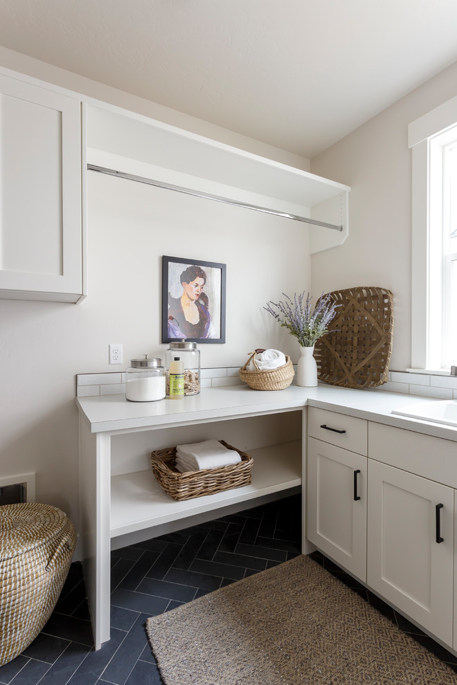 Design ideas for a country l-shaped dedicated laundry room in Boise with a drop-in sink, shaker cabinets, white cabinets, grey walls, black floor and grey benchtop.