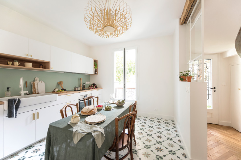 This is an example of a large single-wall open plan kitchen in Paris with a double-bowl sink, flat-panel cabinets, white cabinets, wood benchtops, green splashback, cement tiles, no island and multi-coloured floor.