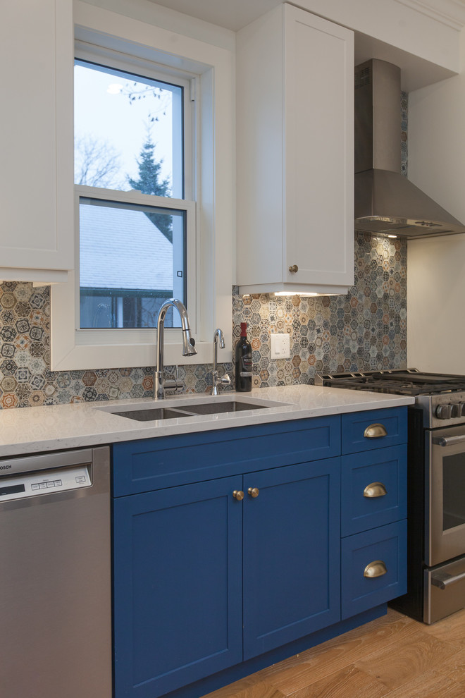 Mid-sized modern eat-in kitchen in Toronto with an undermount sink, shaker cabinets, blue cabinets, granite benchtops, multi-coloured splashback, glass sheet splashback, stainless steel appliances, light hardwood floors, with island and white benchtop.