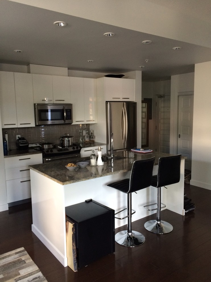 Example of a small transitional galley dark wood floor and brown floor eat-in kitchen design in Edmonton with flat-panel cabinets, white cabinets, granite countertops, an island, an undermount sink, gray backsplash, ceramic backsplash and stainless steel appliances