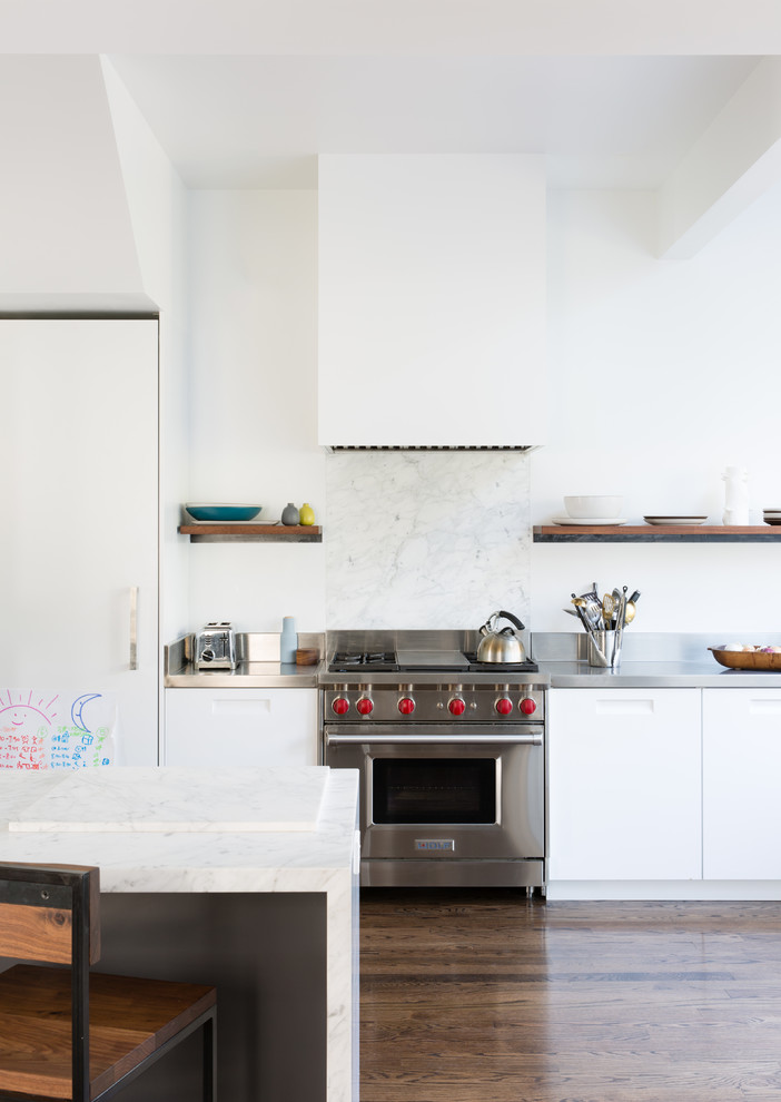Inspiration for a large eclectic galley eat-in kitchen in San Francisco with a drop-in sink, flat-panel cabinets, white cabinets, stainless steel benchtops, white splashback, marble splashback, stainless steel appliances, medium hardwood floors, with island and brown floor.