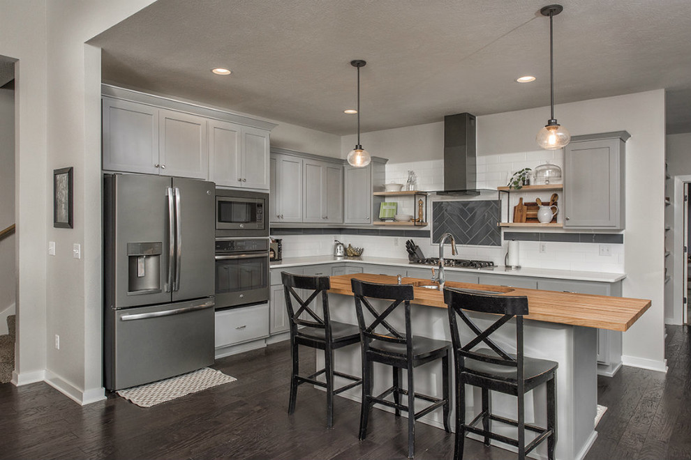 Mid-sized transitional l-shaped dark wood floor and brown floor kitchen photo with an undermount sink, shaker cabinets, gray cabinets, wood countertops, white backsplash, subway tile backsplash, stainless steel appliances and an island