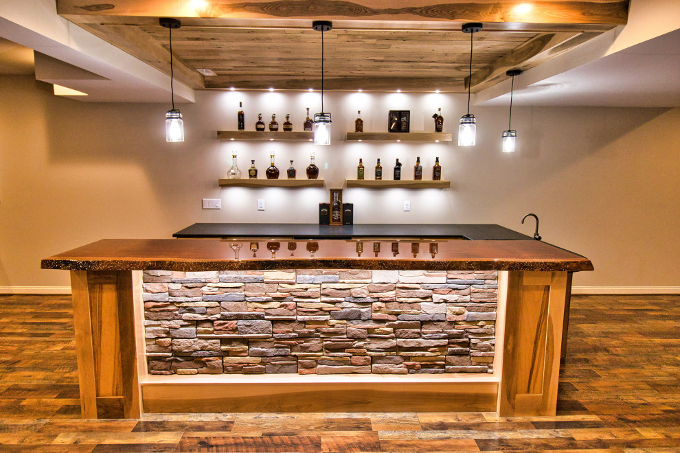 Large country u-shaped wet bar in Cincinnati with an undermount sink, shaker cabinets, light wood cabinets, granite benchtops, laminate floors, brown floor and black benchtop.