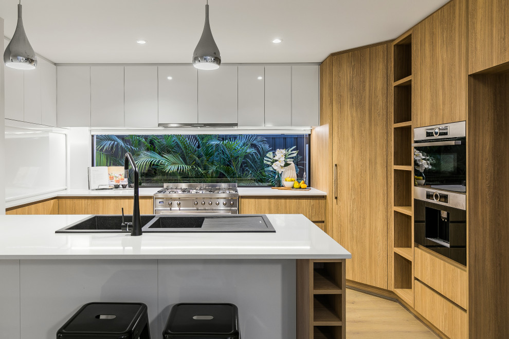Inspiration for a contemporary u-shaped kitchen in Perth with a double-bowl sink, flat-panel cabinets, light wood cabinets, window splashback, light hardwood floors, beige floor and white benchtop.