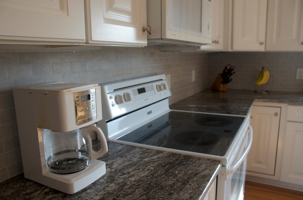 Example of a mid-sized transitional u-shaped medium tone wood floor kitchen design with an undermount sink, flat-panel cabinets, white cabinets, granite countertops, gray backsplash, subway tile backsplash, white appliances and an island