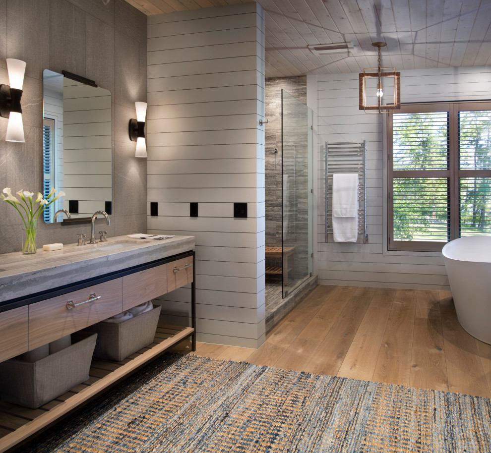 Country master bathroom in Other with a freestanding tub, an undermount sink, a hinged shower door, light wood cabinets, an alcove shower, gray tile, grey walls, medium hardwood floors, brown floor, grey benchtops and flat-panel cabinets.