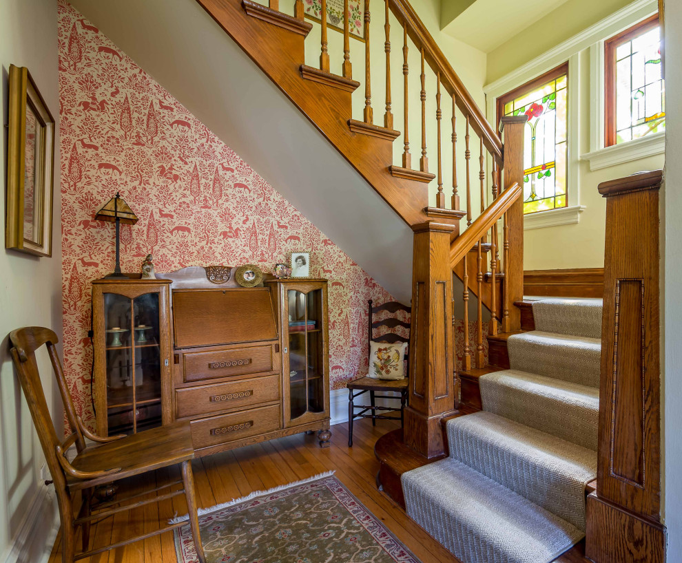 На фото: п-образная деревянная лестница среднего размера в викторианском стиле с ступенями с ковровым покрытием, деревянными перилами и обоями на стенах