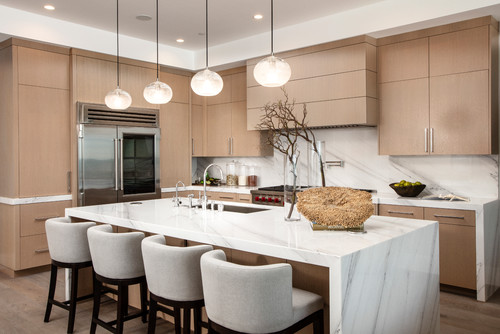 Modern kitchen with light oak slab cabinet doors, minimalist bar pulls, panel-ready fridge, white waterfall marble island, globe pendants, and upholstered stools
