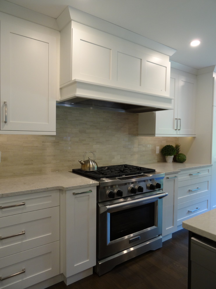 This is an example of a large traditional l-shaped open plan kitchen in Other with a submerged sink, shaker cabinets, white cabinets, engineered stone countertops, grey splashback, marble splashback, stainless steel appliances, medium hardwood flooring, an island and brown floors.