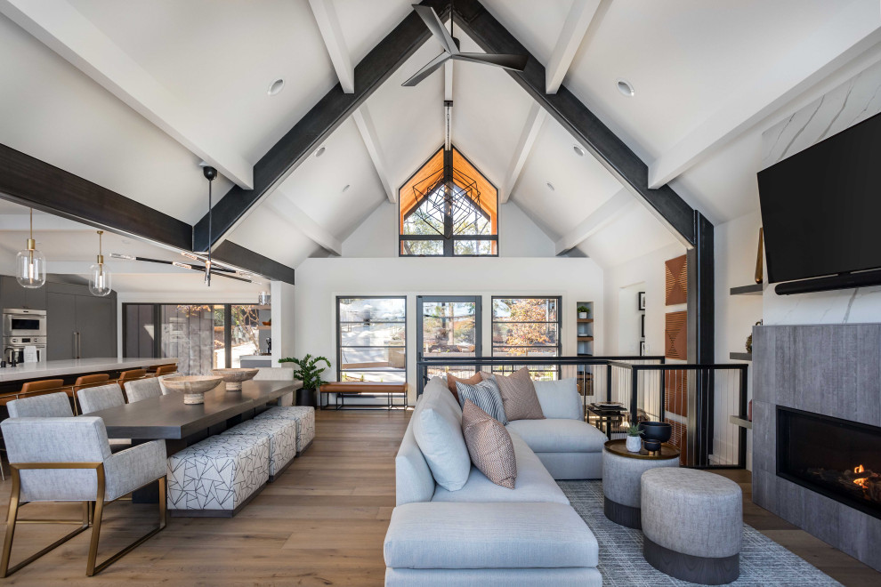 This is an example of a mid-sized contemporary open concept living room in Sacramento with white walls, medium hardwood floors, a standard fireplace, a tile fireplace surround, a wall-mounted tv, brown floor and exposed beam.