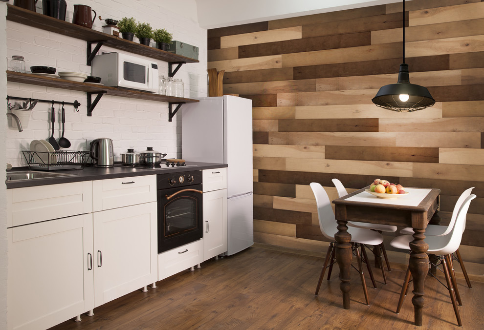 Eat-in kitchen - large transitional dark wood floor and brown floor eat-in kitchen idea with recessed-panel cabinets, white cabinets, white backsplash, brick backsplash, white appliances, no island and black countertops