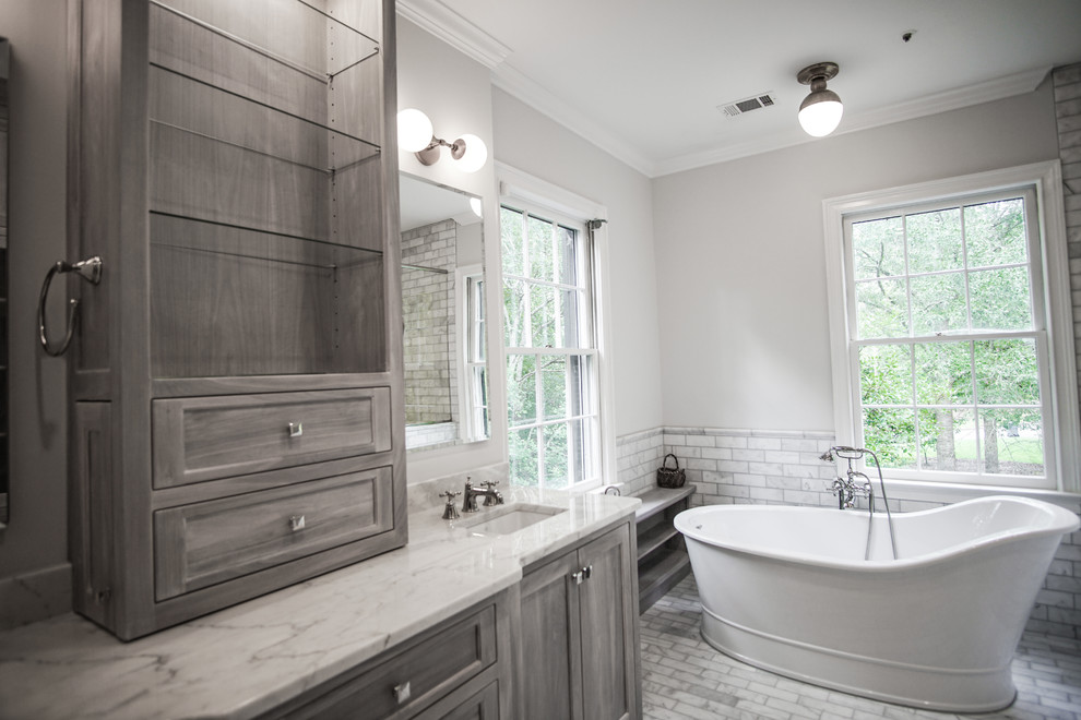 Inspiration for a large traditional master bathroom in Atlanta with shaker cabinets, grey cabinets, a freestanding tub, a curbless shower, a one-piece toilet, gray tile, marble, white walls, marble floors, an undermount sink, marble benchtops, grey floor, a hinged shower door and white benchtops.