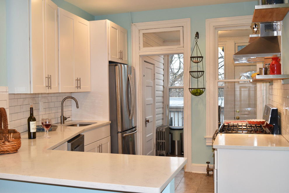 Photo of a mid-sized transitional l-shaped separate kitchen in Baltimore with quartz benchtops, subway tile splashback, an undermount sink, shaker cabinets, white cabinets, white splashback, stainless steel appliances, ceramic floors, a peninsula and brown floor.