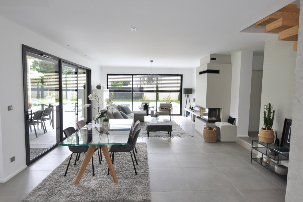 Example of a large trendy open concept gray floor, concrete floor and tray ceiling living room design in Lyon with a standard fireplace, a tv stand and white walls