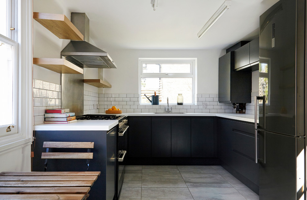 This is an example of a contemporary u-shaped kitchen in London with a drop-in sink, flat-panel cabinets, black cabinets, white splashback, subway tile splashback, black appliances and no island.