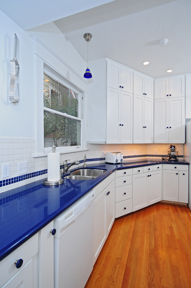 Mid-sized transitional u-shaped medium tone wood floor kitchen pantry photo in Seattle with a double-bowl sink, shaker cabinets, white cabinets, solid surface countertops, blue backsplash, ceramic backsplash, white appliances, white walls and no island