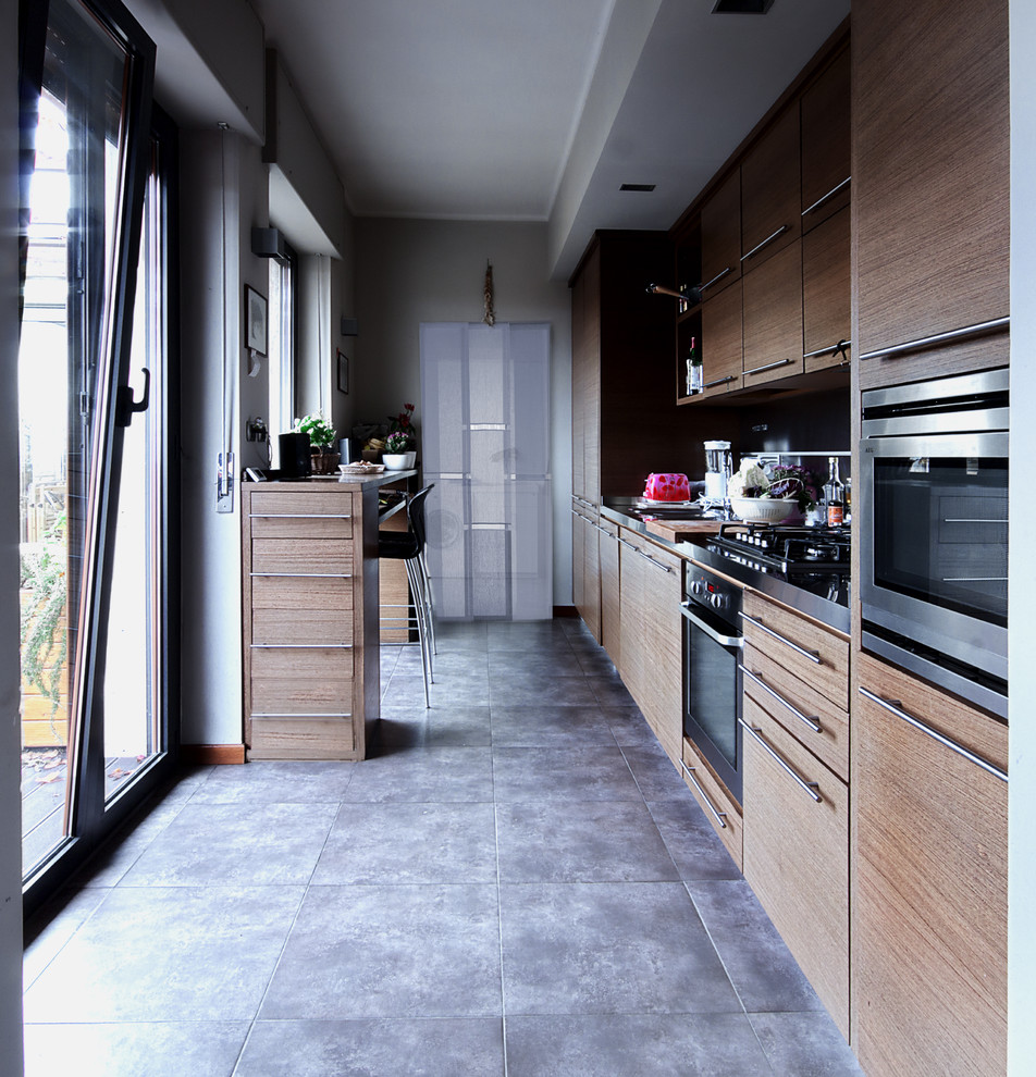 Design ideas for a mid-sized contemporary galley separate kitchen in Turin with a drop-in sink, flat-panel cabinets, dark wood cabinets, stainless steel benchtops, mirror splashback, stainless steel appliances, porcelain floors and no island.