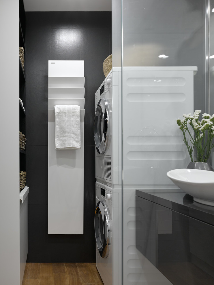 This is an example of a contemporary laundry room in Moscow with black walls and a stacked washer and dryer.
