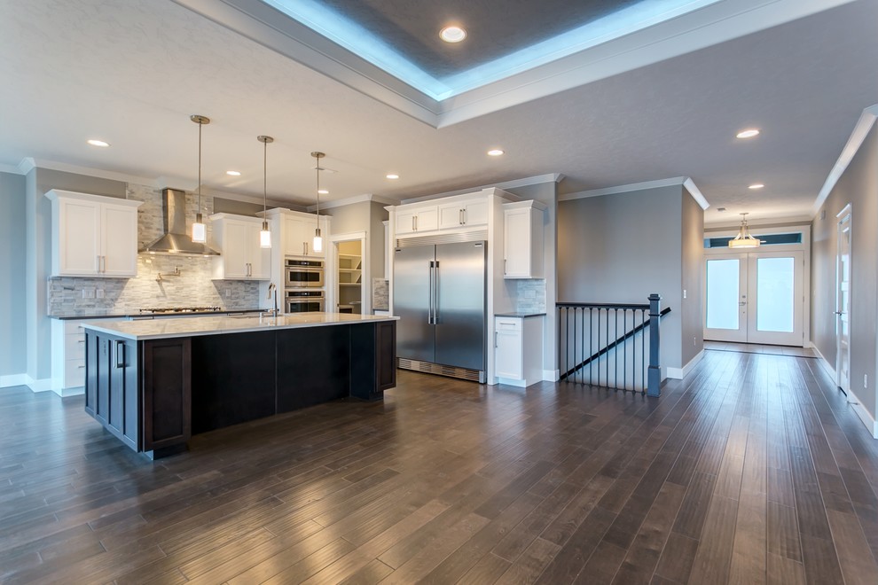 Open concept kitchen - mid-sized transitional l-shaped medium tone wood floor open concept kitchen idea in Seattle with an undermount sink, shaker cabinets, white cabinets, quartz countertops, gray backsplash, stone tile backsplash, stainless steel appliances and an island