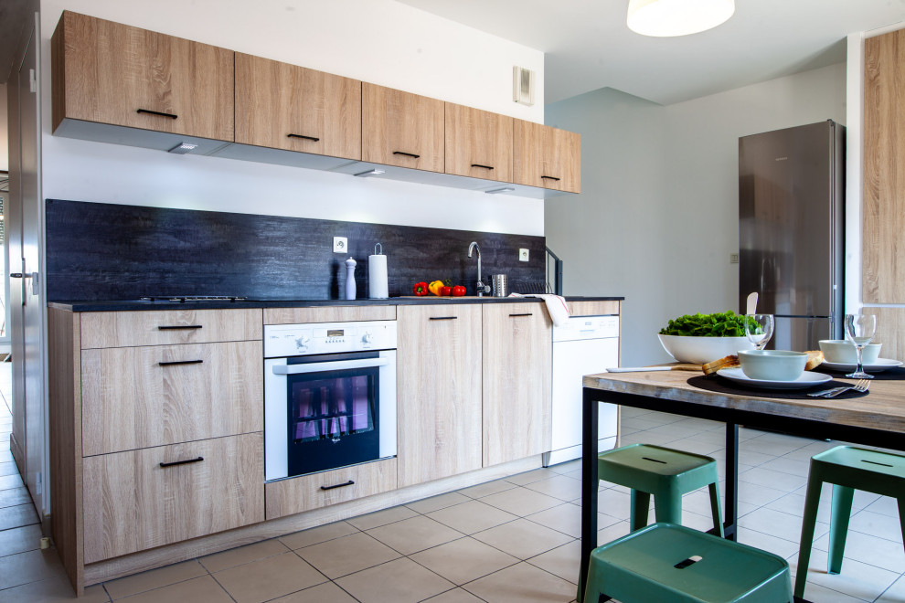 This is an example of a mid-sized industrial l-shaped separate kitchen in Lyon with a single-bowl sink, flat-panel cabinets, light wood cabinets, laminate benchtops, black splashback and black benchtop.