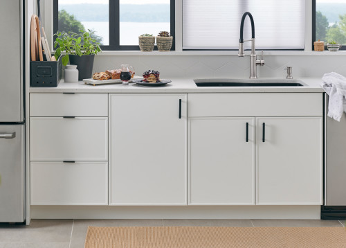 Skinny Shaker cabinet fronts—matte white with thin 1/2–3/4 inch rails, black hardware, drawers and doors beneath a window sink