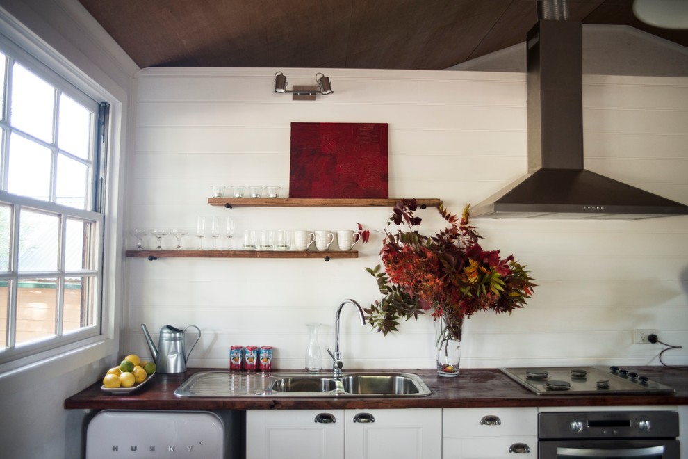 Photo of a mid-sized industrial single-wall eat-in kitchen in Melbourne with a double-bowl sink, open cabinets, white cabinets, wood benchtops, white splashback, stainless steel appliances, concrete floors and with island.