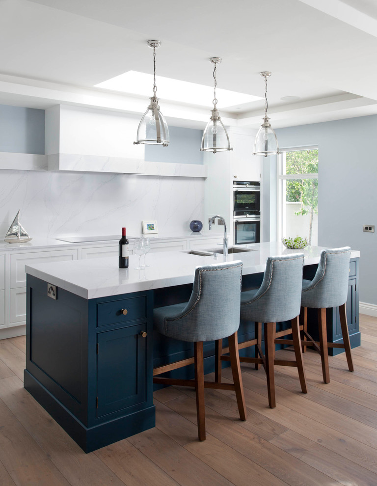 Transitional dark wood floor and brown floor kitchen photo in Dublin with a double-bowl sink, recessed-panel cabinets, white cabinets, white backsplash, stainless steel appliances and an island