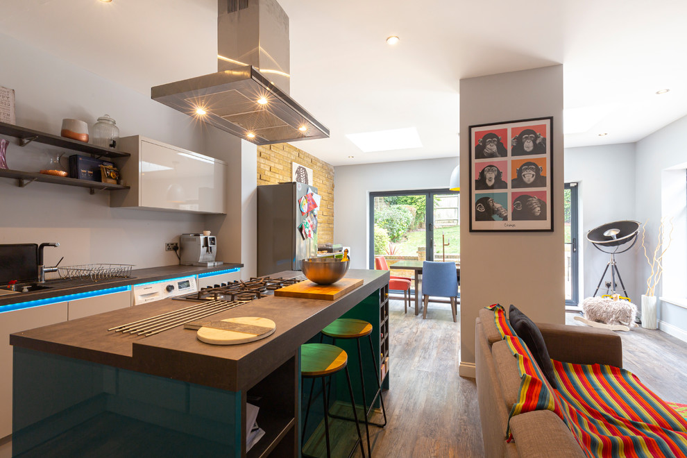 This is an example of a mid-sized contemporary l-shaped open plan kitchen in London with dark hardwood floors, brown floor, an integrated sink, flat-panel cabinets, grey cabinets, terrazzo benchtops, white appliances, with island and grey benchtop.
