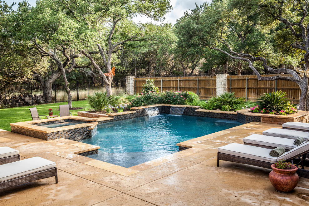 This is an example of a mid-sized traditional backyard custom-shaped lap pool in Austin with a water feature and stamped concrete.
