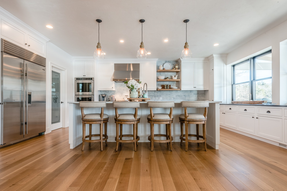 Inspiration for a large traditional u-shaped open plan kitchen in Bridgeport with a farmhouse sink, recessed-panel cabinets, white cabinets, granite benchtops, marble splashback, stainless steel appliances, medium hardwood floors, with island, brown floor and grey benchtop.