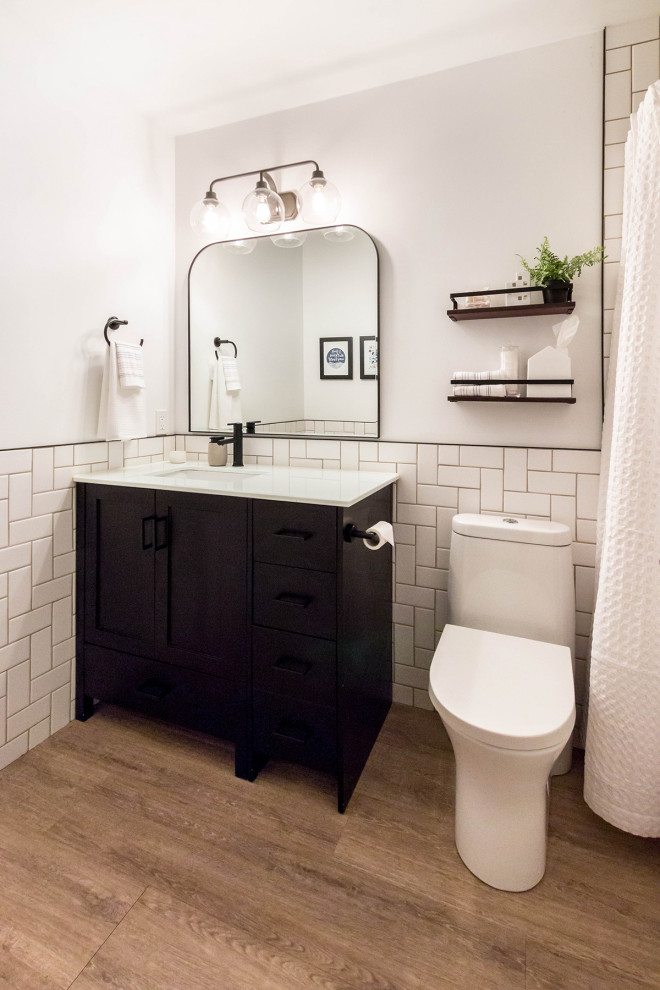 Свежая идея для дизайна: маленькая ванная комната в стиле модернизм с фасадами в стиле шейкер, черными фасадами, ванной в нише, душем над ванной, унитазом-моноблоком, белой плиткой, керамической плиткой, белыми стенами, полом из винила, врезной раковиной, столешницей из искусственного камня, коричневым полом, шторкой для ванной, белой столешницей, нишей, тумбой под одну раковину, напольной тумбой и панелями на стенах для на участке и в саду - отличное фото интерьера