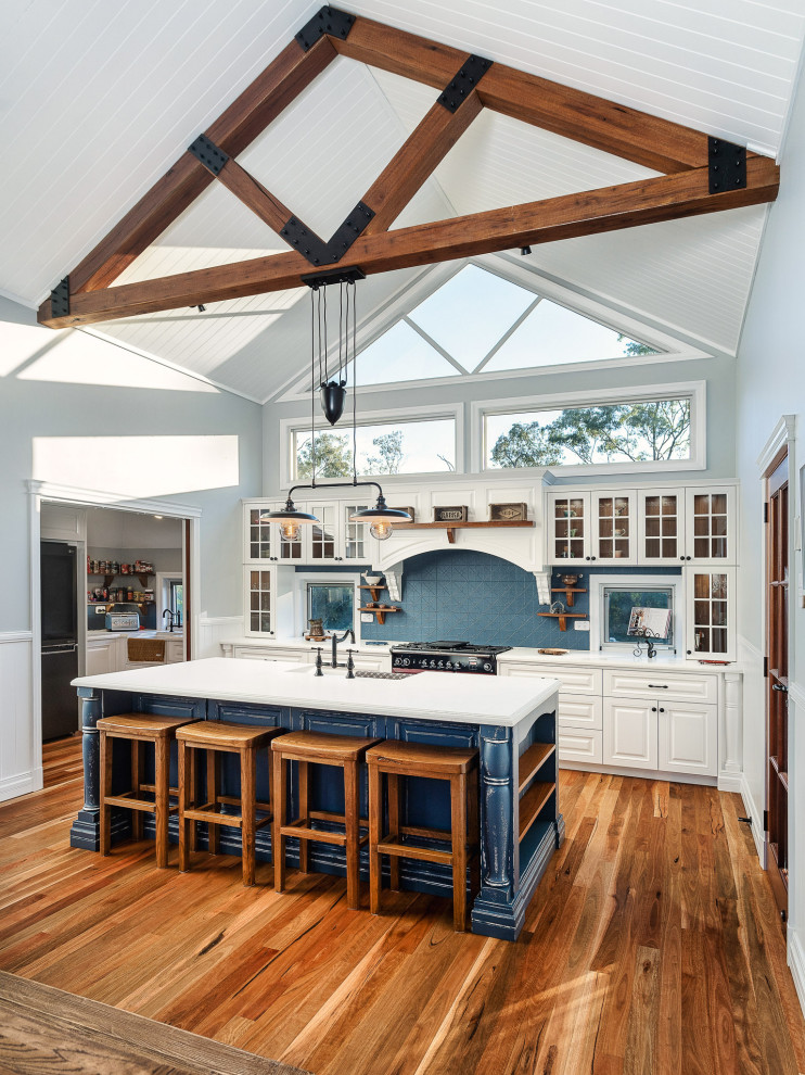 Inspiration for a medium sized farmhouse galley open plan kitchen in Brisbane with a belfast sink, shaker cabinets, white cabinets, engineered stone countertops, blue splashback, ceramic splashback, coloured appliances, light hardwood flooring, brown floors, white worktops and exposed beams.