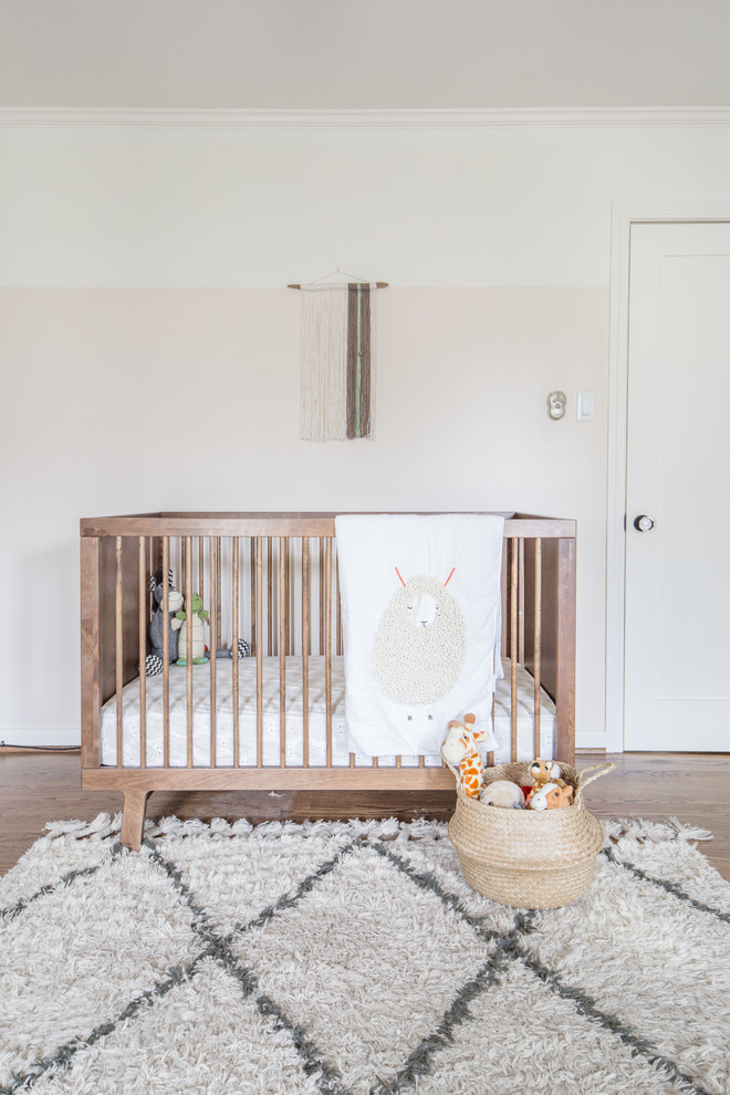 This is an example of a transitional nursery for girls in Houston with pink walls and medium hardwood floors.