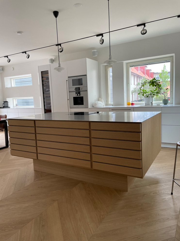 This is an example of a mid-sized scandinavian single-wall eat-in kitchen in Malmo with a single-bowl sink, louvered cabinets, light wood cabinets, stainless steel benchtops, panelled appliances, light hardwood floors and with island.