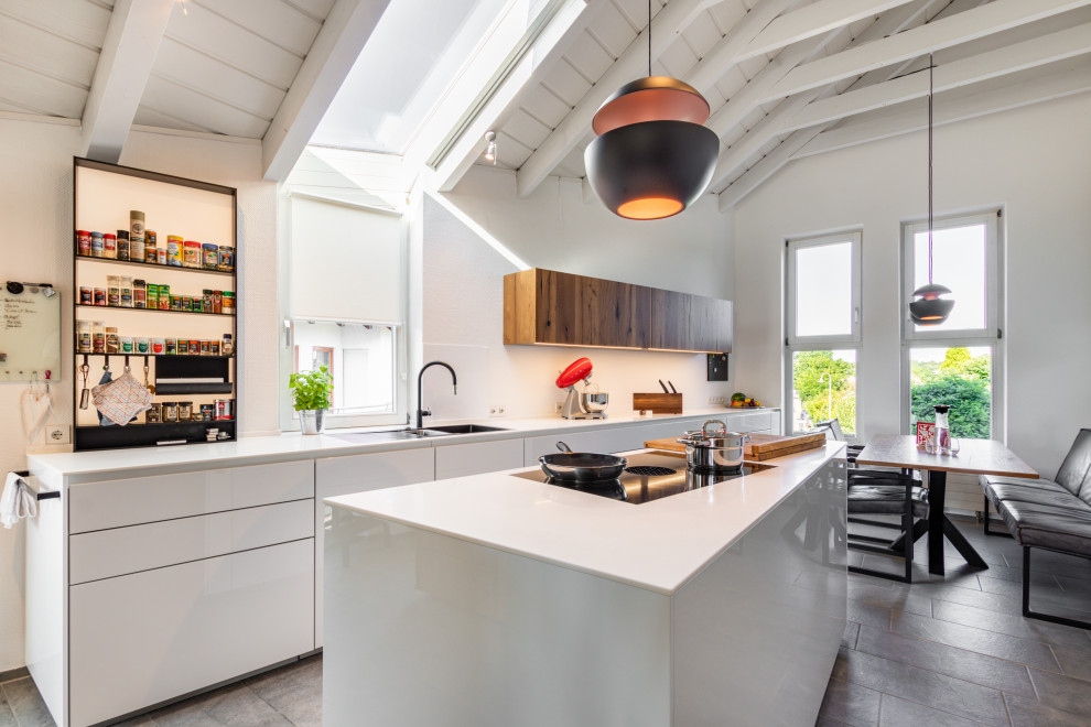 Design ideas for a large modern galley eat-in kitchen in Stuttgart with an integrated sink, flat-panel cabinets, white cabinets, solid surface benchtops, black appliances, ceramic floors, with island, grey floor, white benchtop and exposed beam.