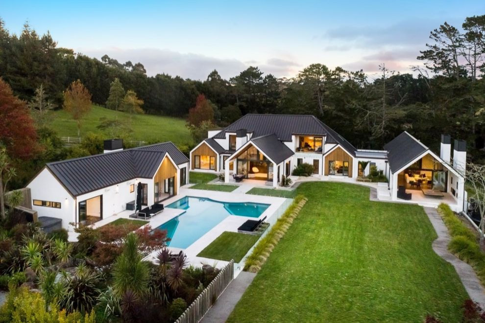 Photo of a large contemporary two-storey adobe white house exterior in Auckland with a gable roof, a metal roof and a black roof.