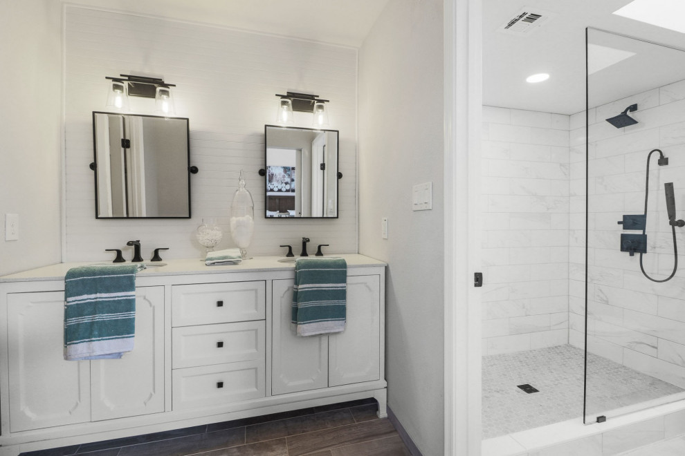 This is an example of a transitional bathroom in Phoenix with white cabinets, an alcove shower, white tile, white walls, wood-look tile, brown floor, white benchtops, a double vanity, a freestanding vanity, recessed-panel cabinets, marble, an undermount sink and a hinged shower door.