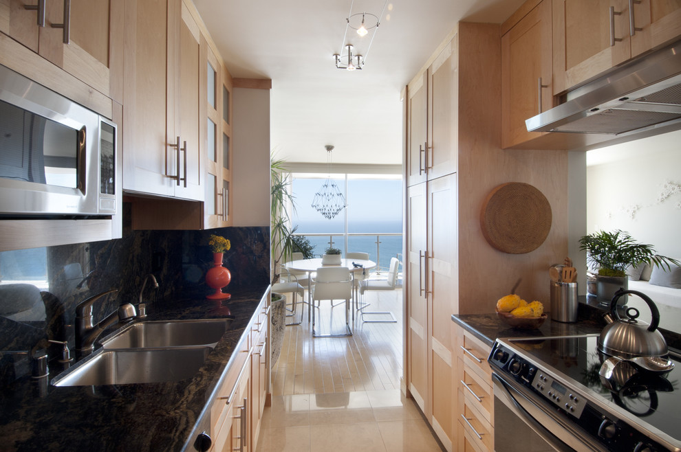 Design ideas for a small contemporary galley open plan kitchen in Los Angeles with a double-bowl sink, shaker cabinets, light wood cabinets, stone slab splashback, stainless steel appliances, no island and black splashback.